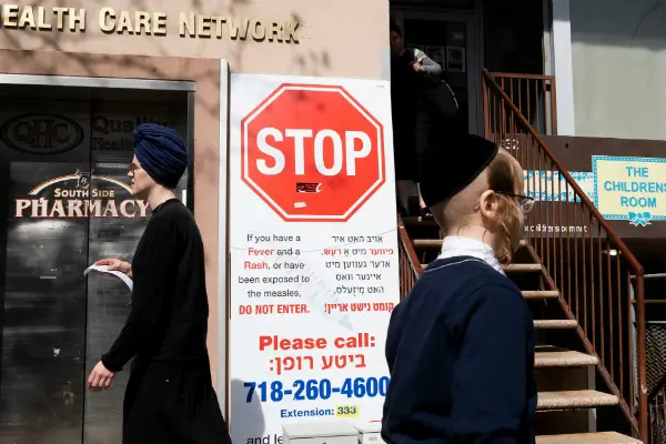 People walk past a sign outside of health clinic with warnings about measles in the Orthodox Jewish area of Williamsburg on April 25